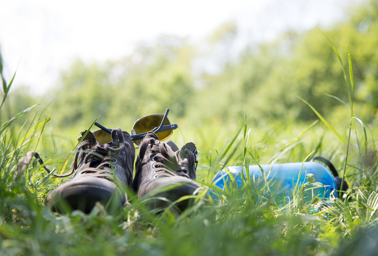 Summer holidays: Blue bottle of water and grey shoes in the gree